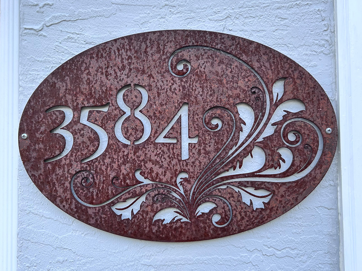 Oval CNC-cut steel address plaque number 3584 with decorative scrollwork and orange rust patina